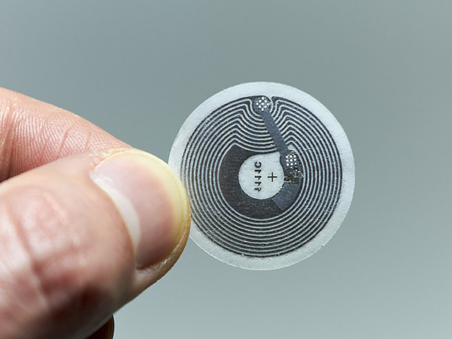 Etiqueta NFC circular sostenida entre dos dedos, del tamaño de una moneda